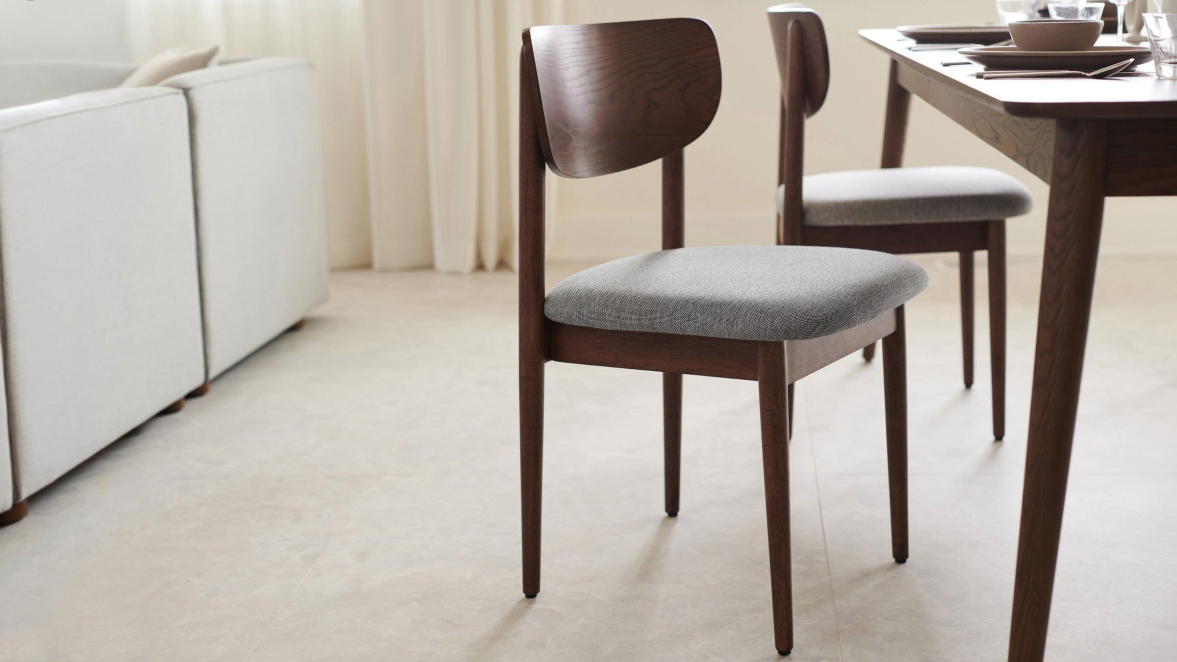 Mid-century modern dining chair with dark wooden frame and light gray cushioned seat in a bright dining room.
