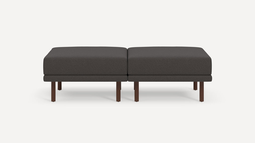 Dark gray upholstered modern rectangular ottoman with wooden legs, consisting of two connected cushioned seats.
