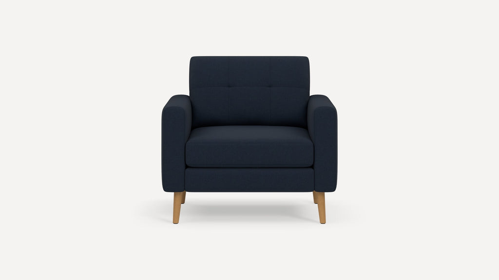 Modern dark navy upholstered armchair with wooden legs, square arms, and subtle button tufting on backrest.