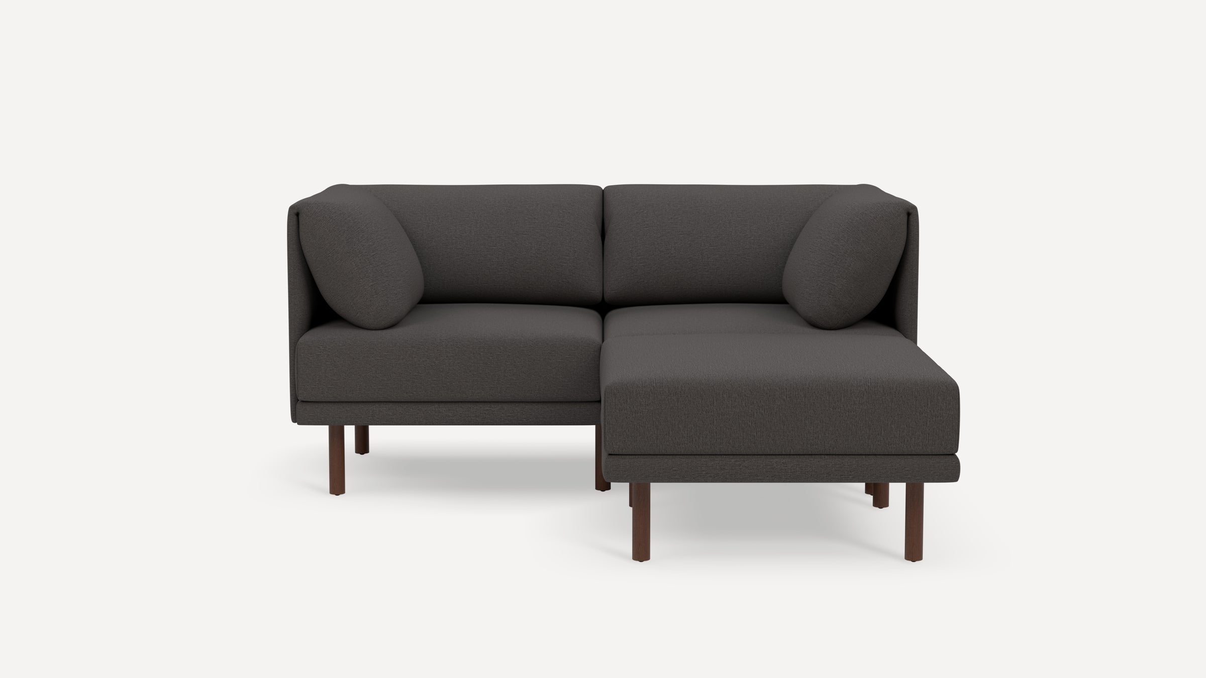 Modern dark gray fabric sectional sofa with chaise lounge, wooden legs, and matching cylindrical cushions on a white background.