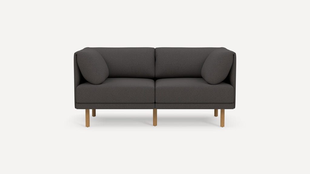 Modern dark gray two-seater sofa with rounded cushions and wooden legs, isolated on a plain white background.