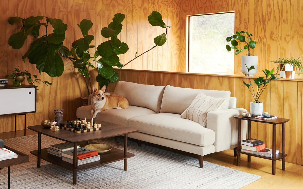a living room with a beige sectional sofa, a wooden coffee table, and a large fiddled plant on the wall