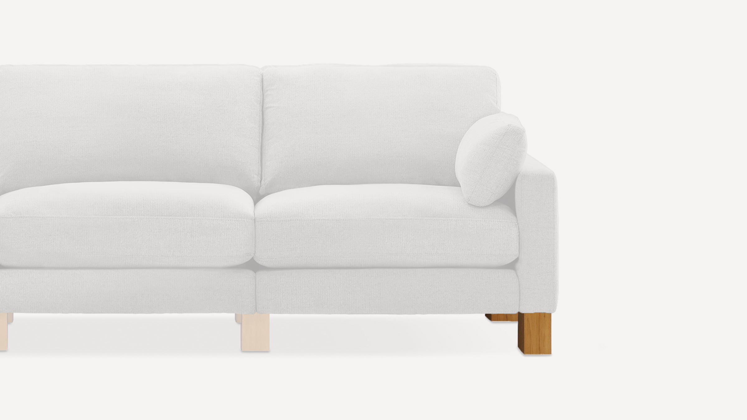 Partial view of a white upholstered loveseat with a matching round pillow on the right armrest and wooden legs.