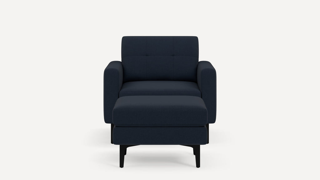 Front view of a modern navy blue armchair with a matching ottoman, featuring soft cushions and black legs, on a white background.