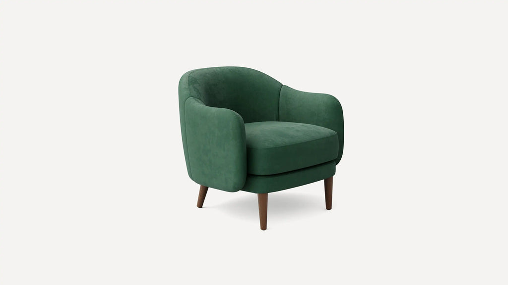 Modern green velvet armchair with rounded backrest and armrests, supported by four tapered wooden legs.