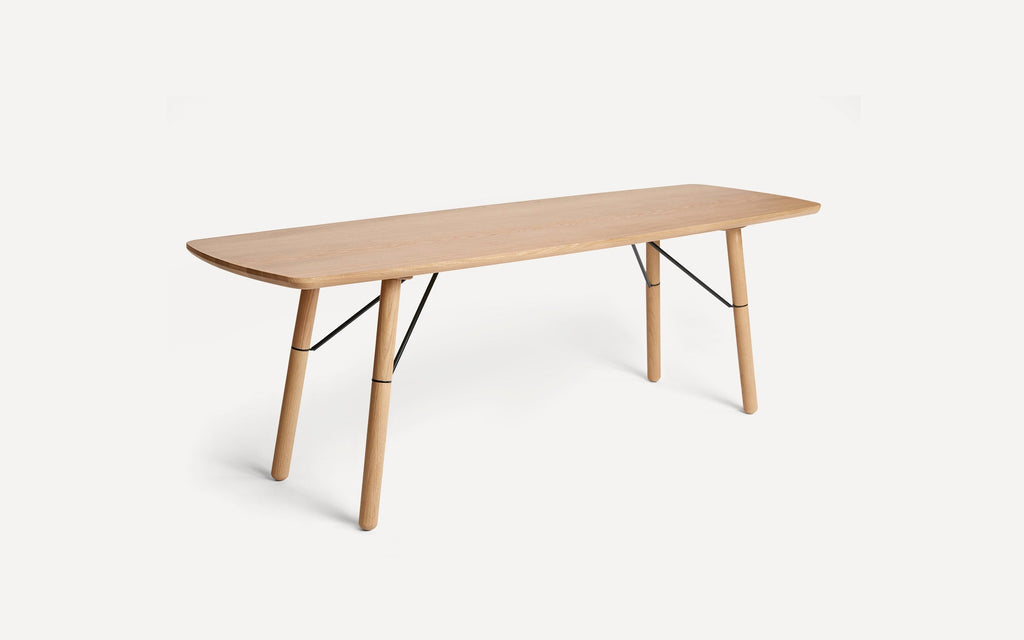 Rectangular wooden dining table with rounded edges, four angled legs, and black metal supports on a white background.