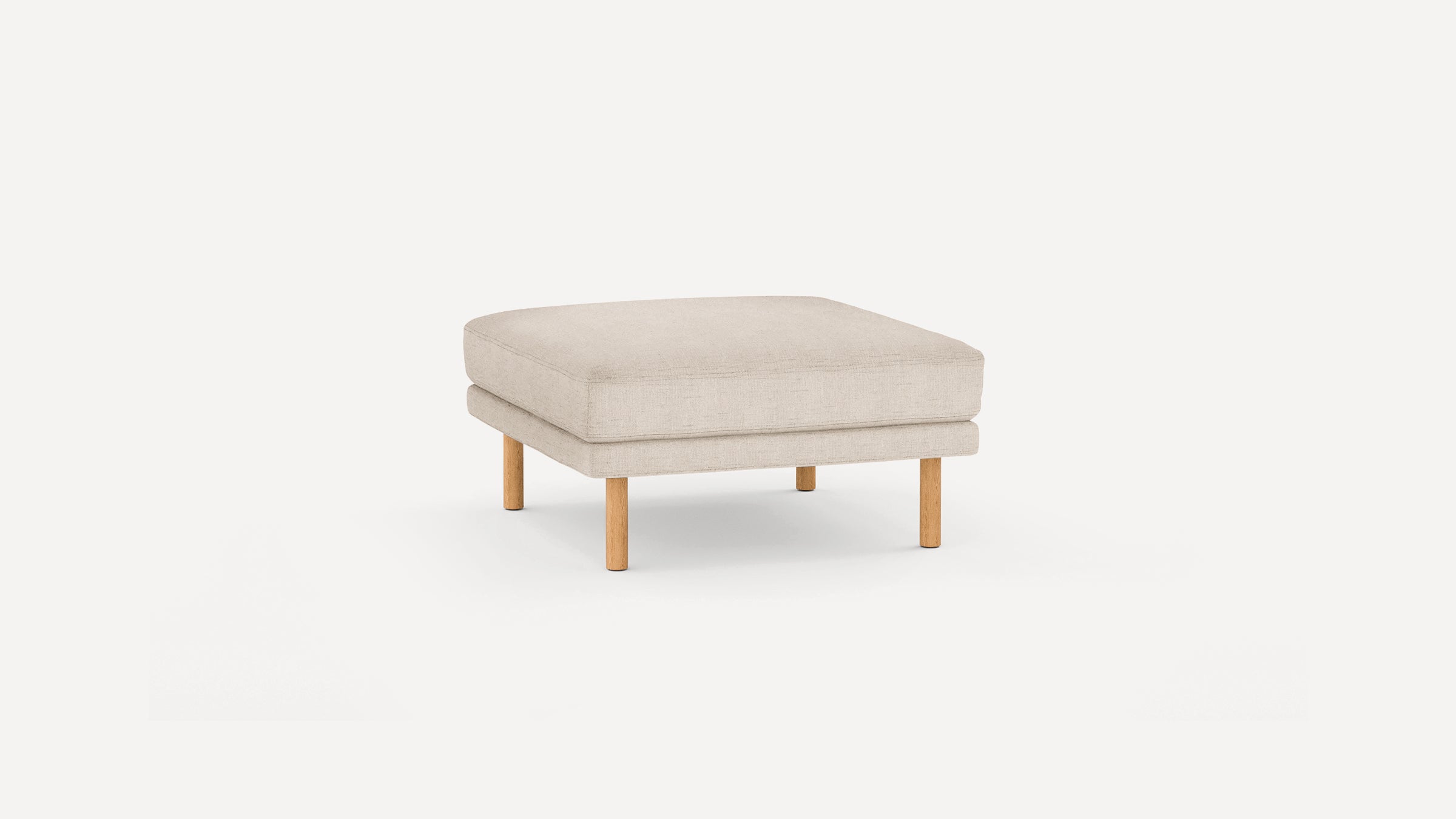 Beige fabric ottoman with thick cushion and four wooden legs, minimalist and modern design on white background.