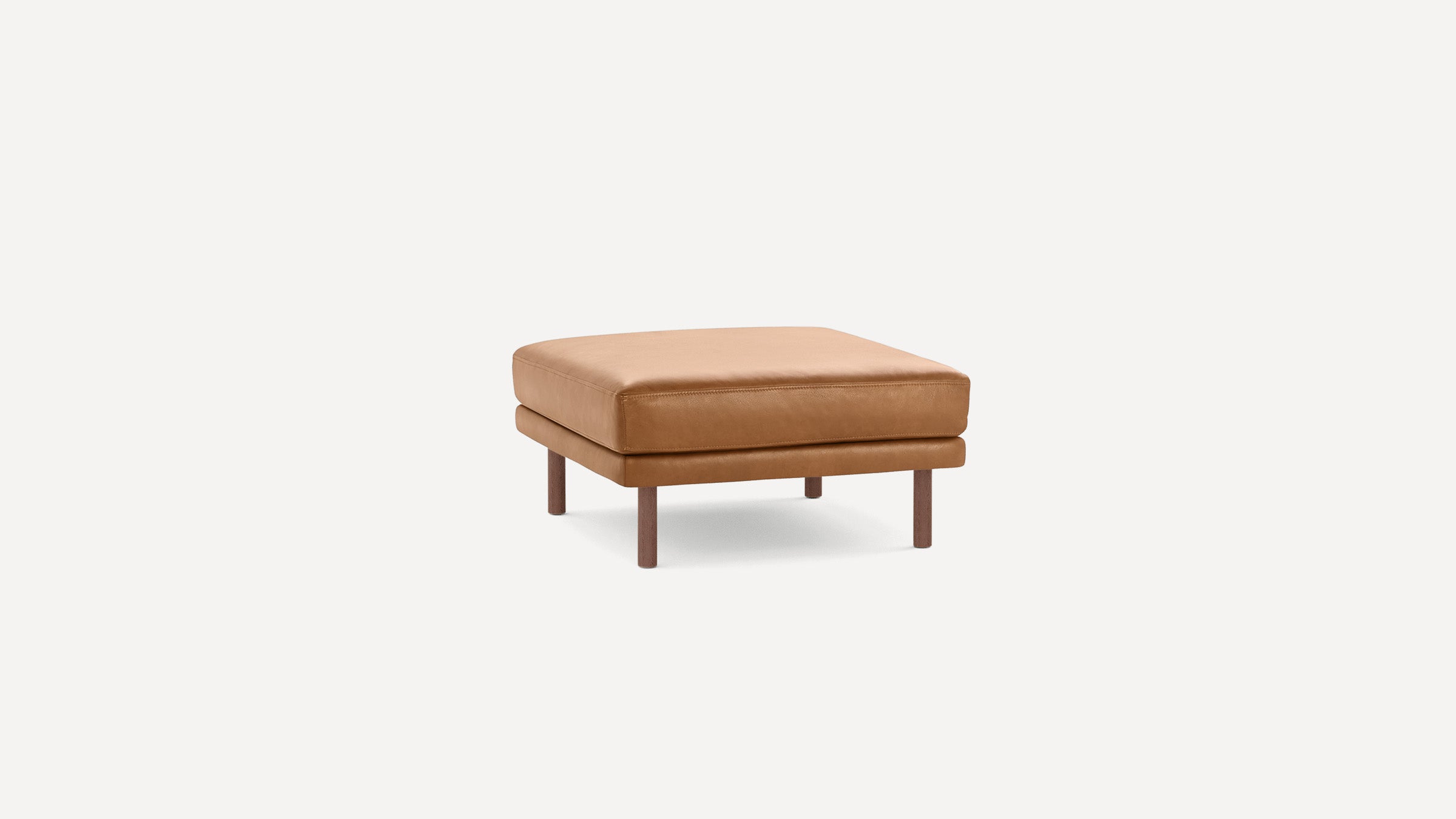 Square tan leather ottoman with cushioned top and four wooden legs on a plain white background.