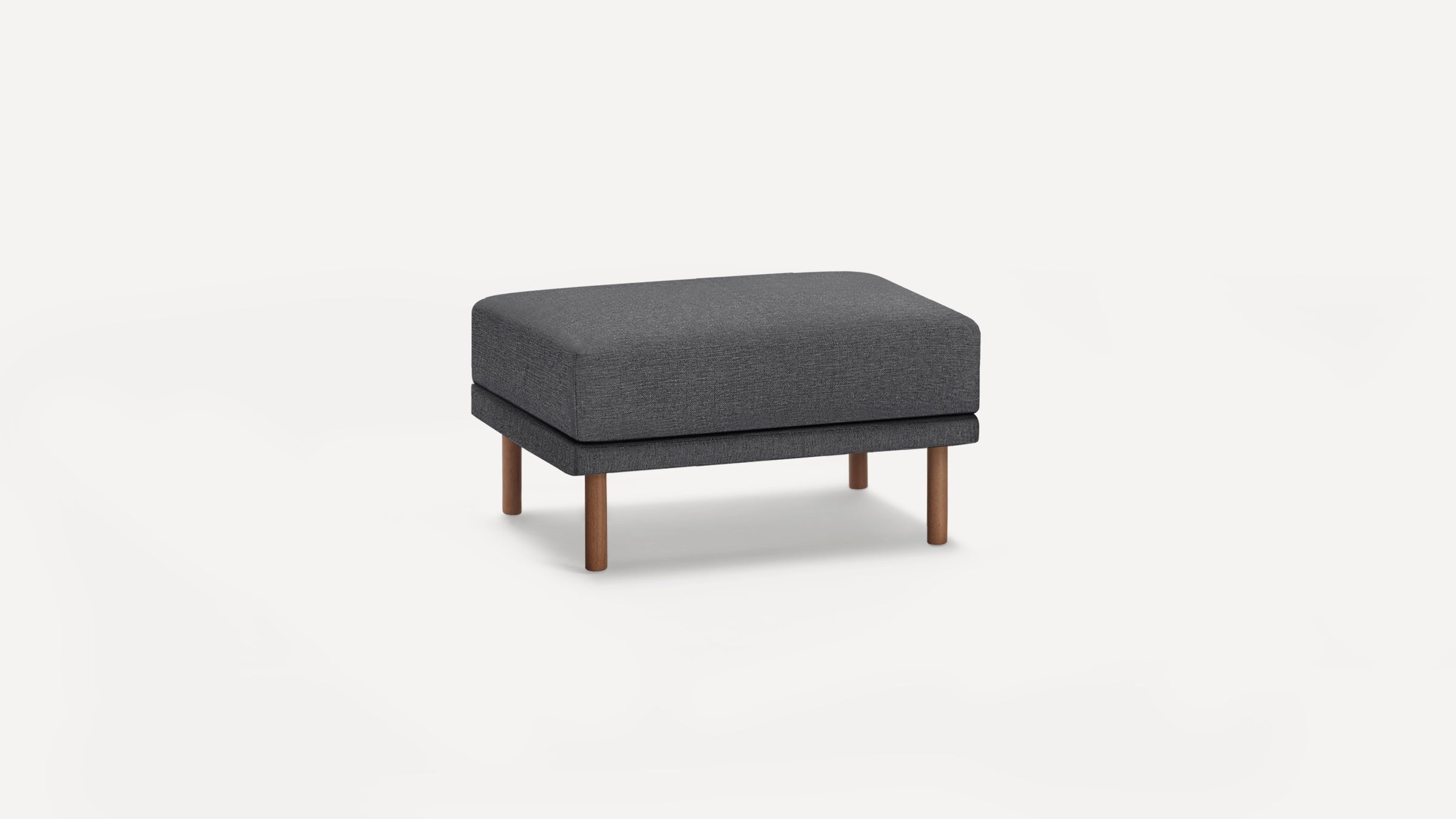 Modern rectangular dark gray fabric ottoman with wooden legs on a white background.