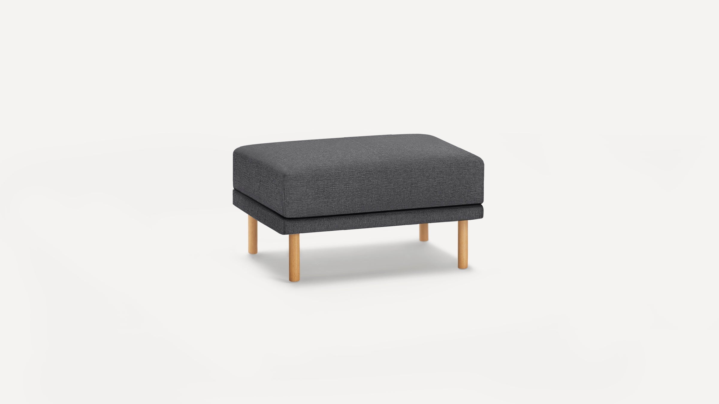 Rectangular dark gray upholstered ottoman with four light wooden legs, minimalistic modern design on white background.