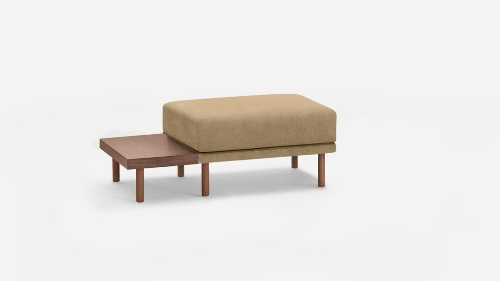 Modern beige cushioned bench with adjacent wooden side table and cylindrical wooden legs on white background.