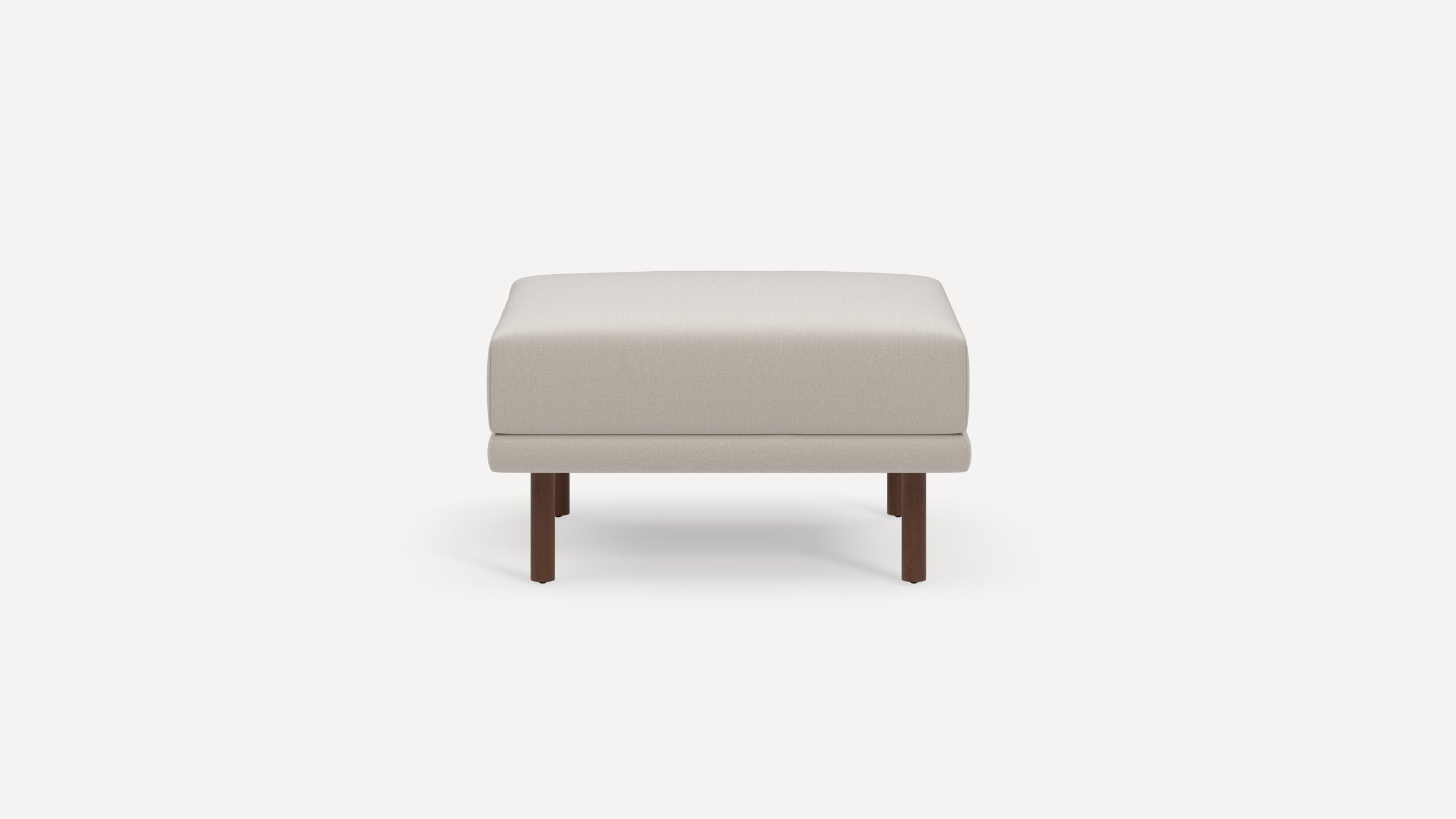 Modern beige upholstered ottoman with a thick cushion and four dark wooden legs on a white background.