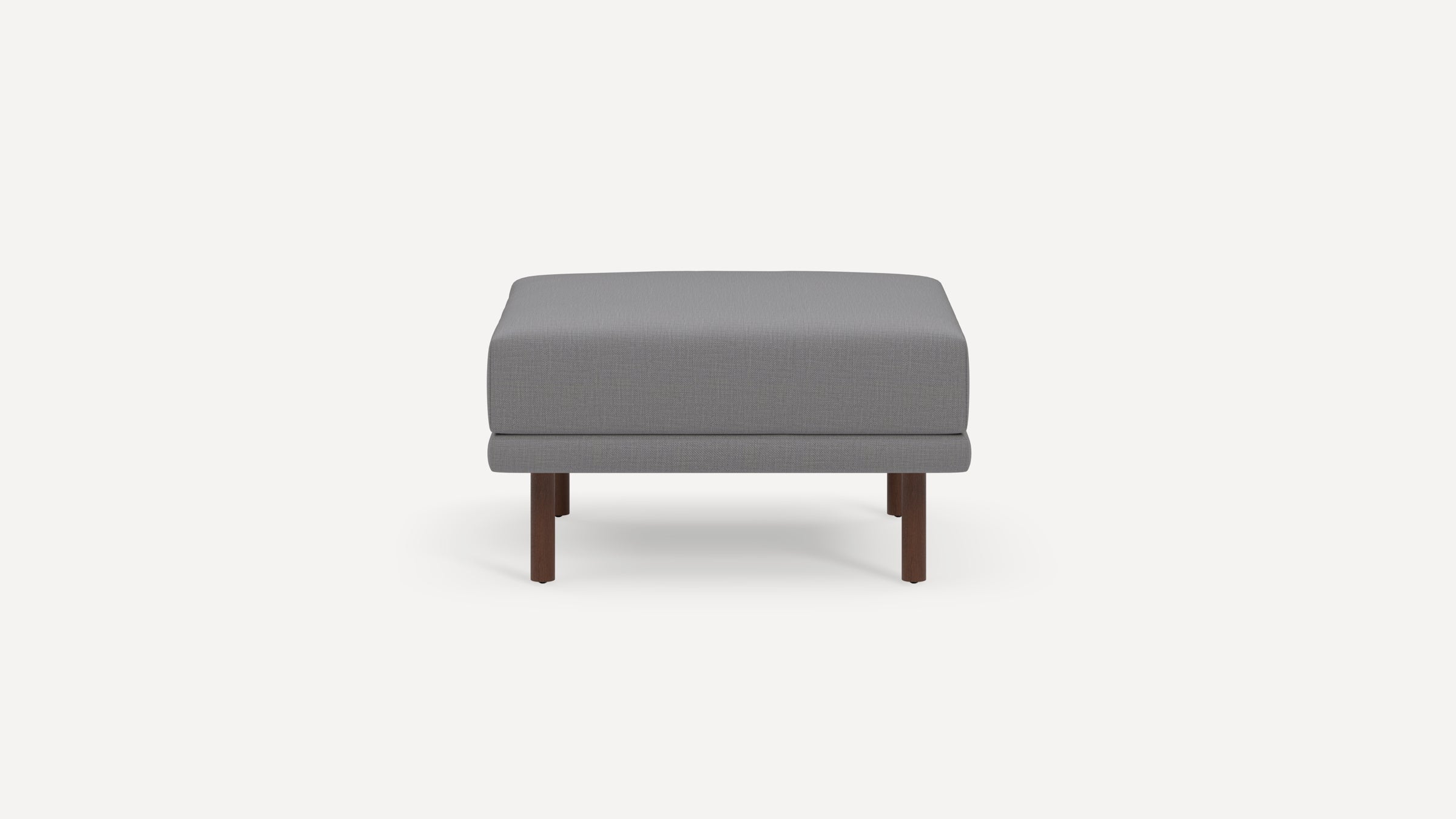 Square gray upholstered ottoman with clean lines, supported by four short wooden legs in a minimalist design.