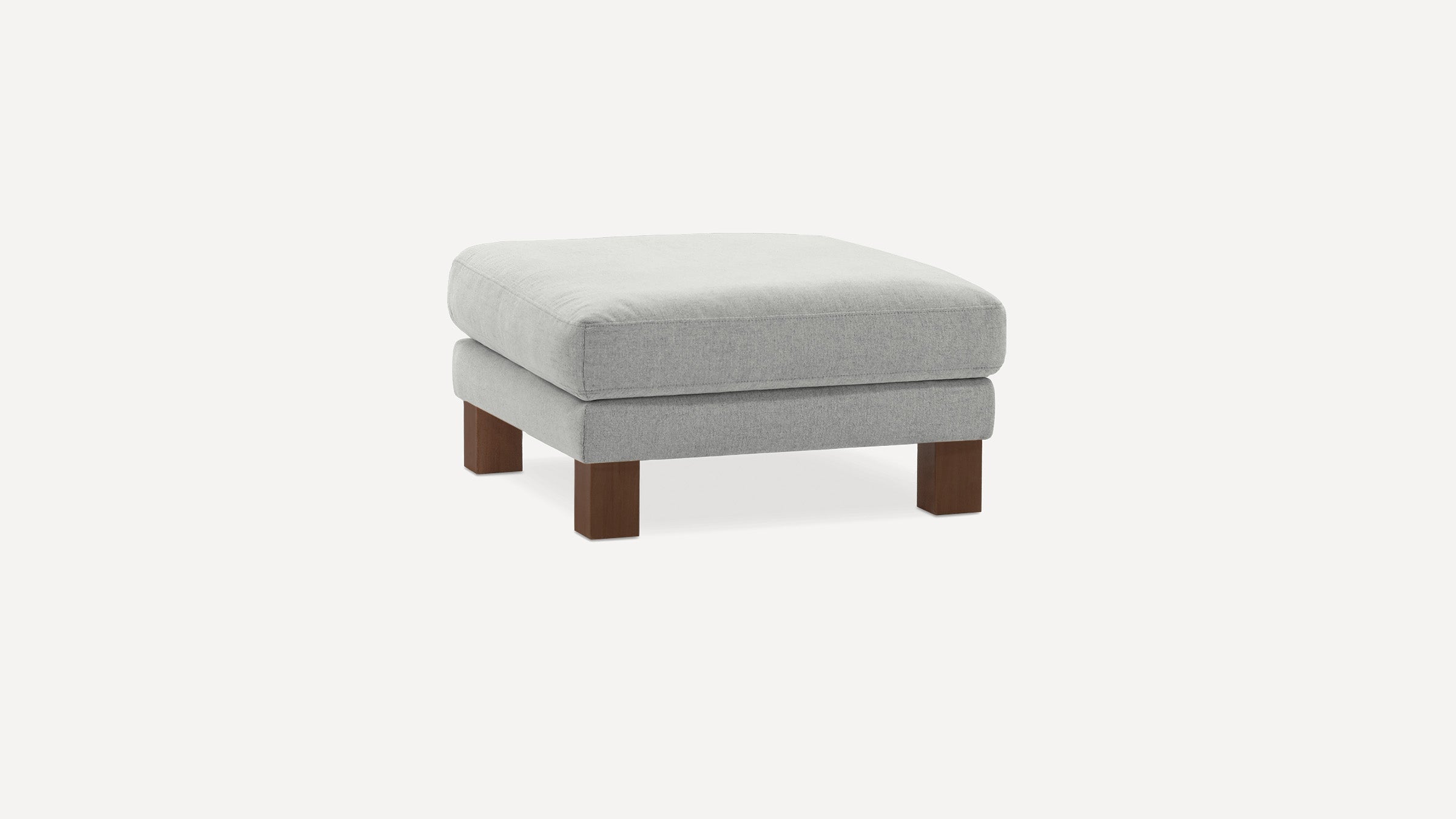Light gray upholstered square ottoman with thick cushioning and dark wooden block legs on a white background.