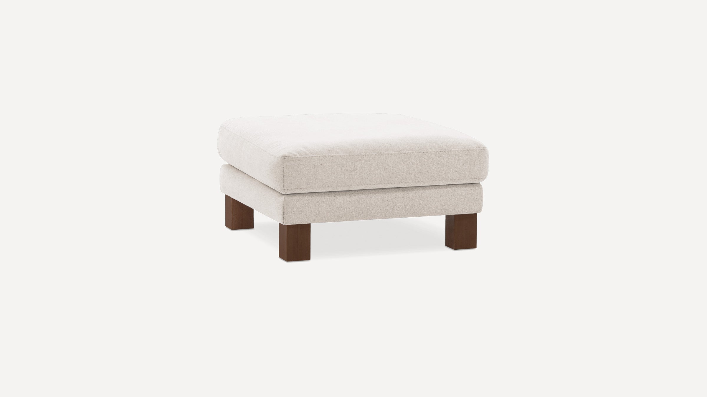 Square beige upholstered ottoman with thick cushion and short dark wooden legs on a white background.