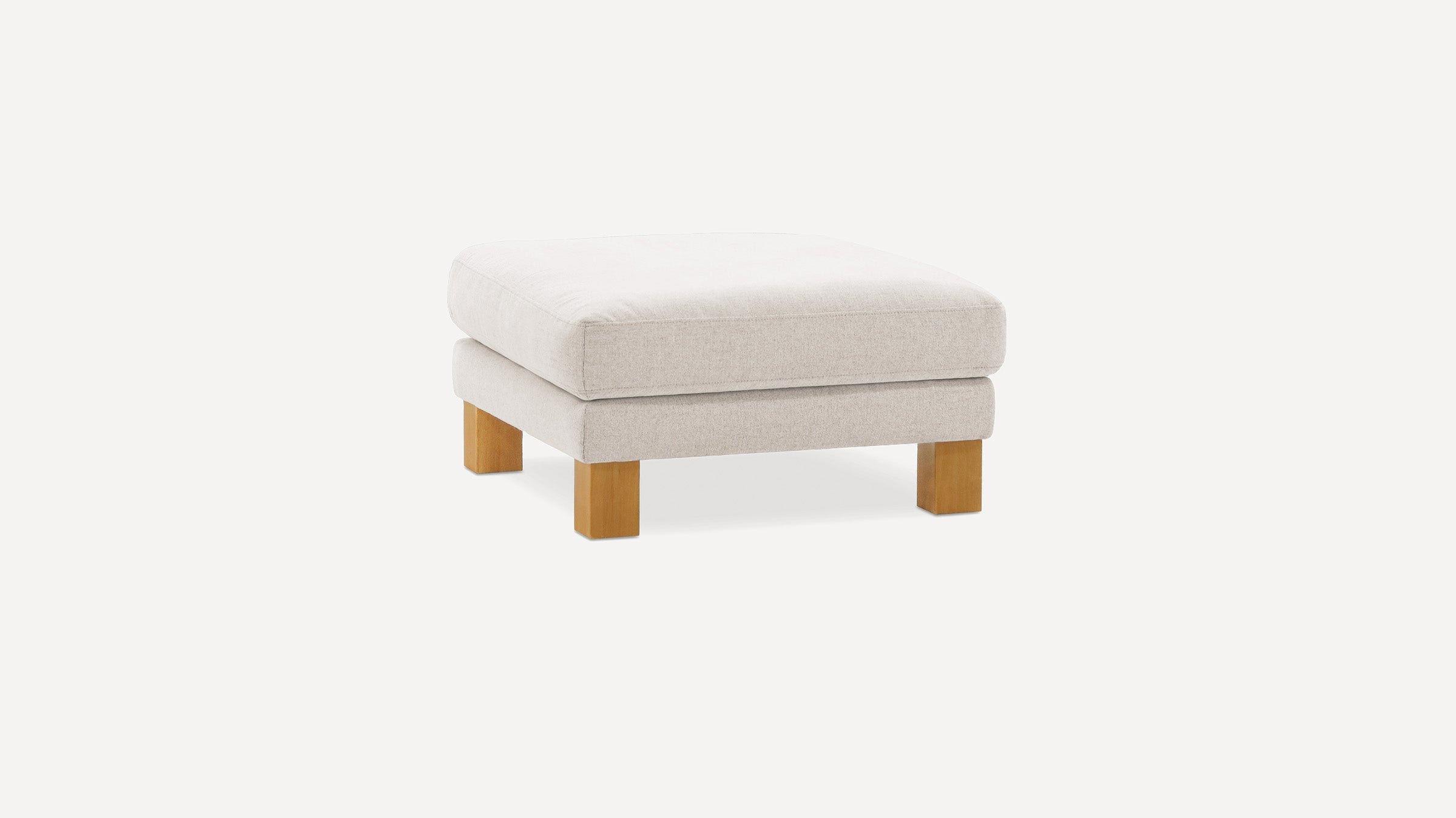 Small, square beige upholstered ottoman with a thick cushion top and four light wooden block legs.