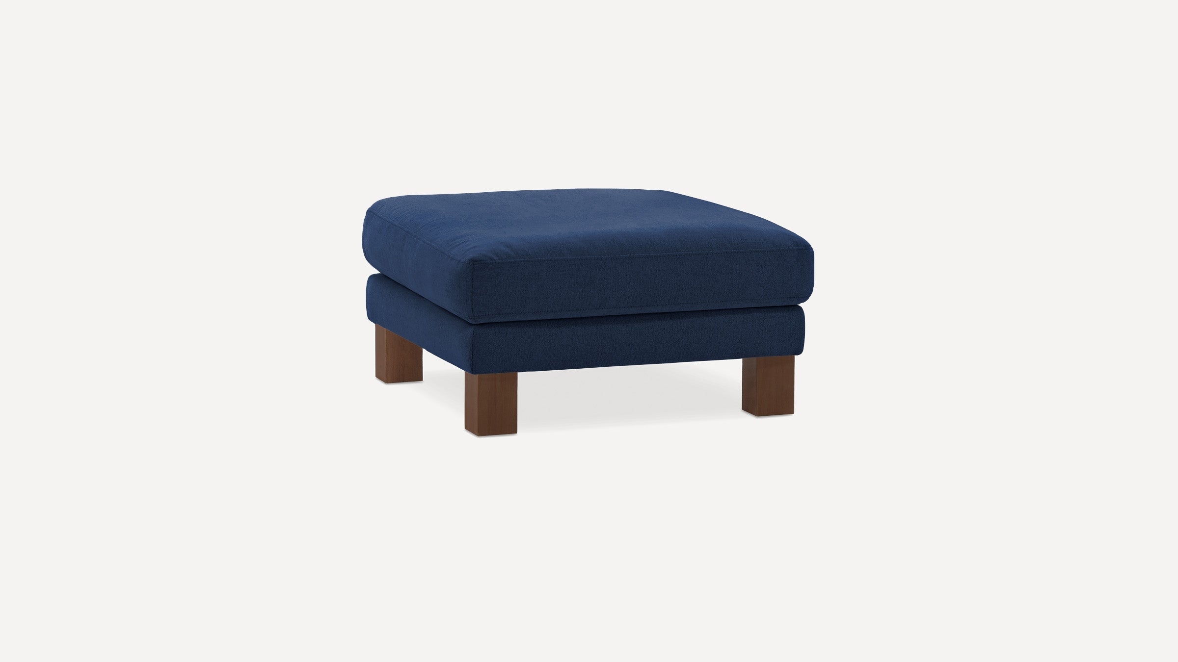 Square navy blue upholstered ottoman with thick cushion and four short wooden legs on a plain white background.