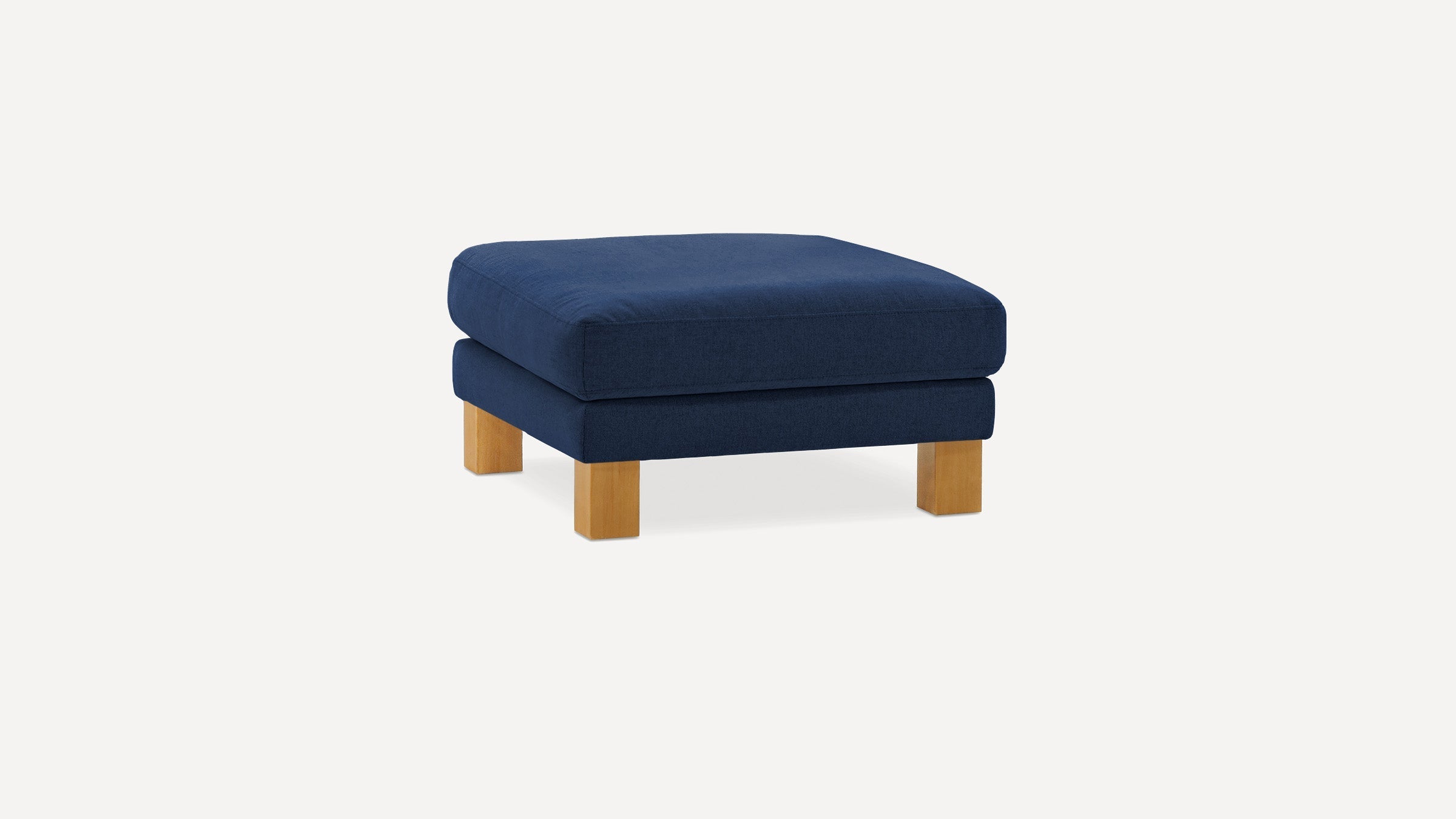 Square navy blue upholstered ottoman with thick cushion top and light wooden block legs on a plain background.