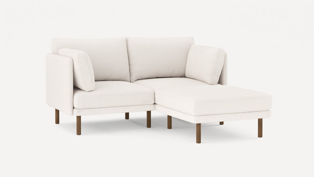 Modern white sectional sofa with textured fabric, wooden legs, and cushioned seats, featuring a chaise lounge on the right side.