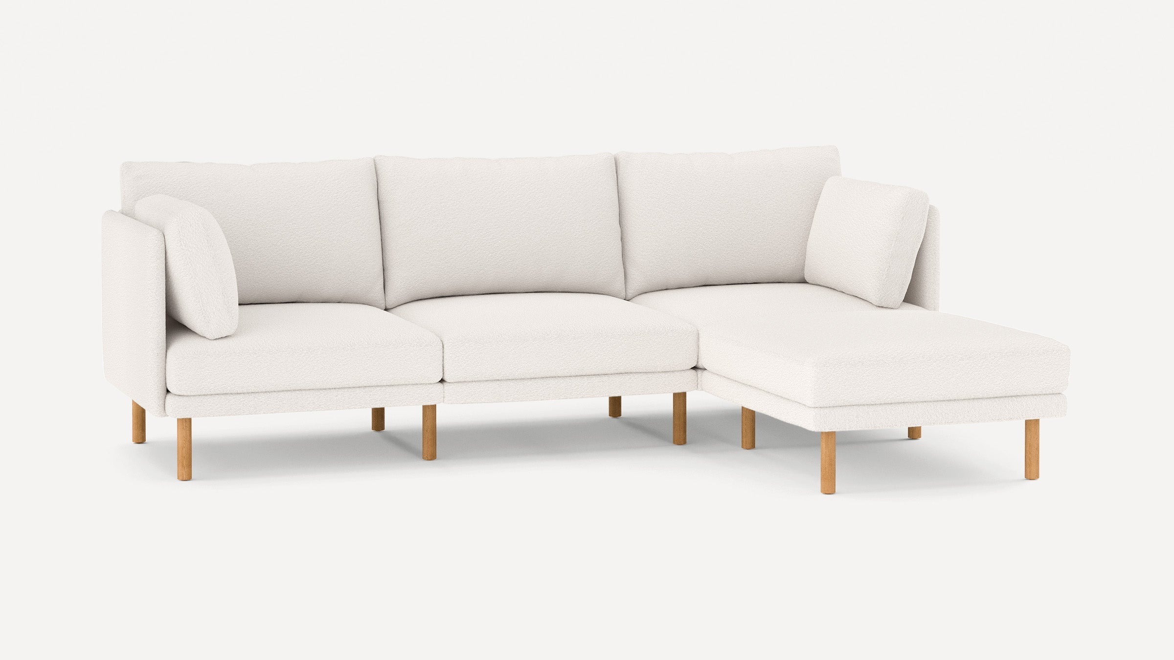 White modern sectional sofa with wooden legs, featuring three back cushions and two side pillows, on a white background.