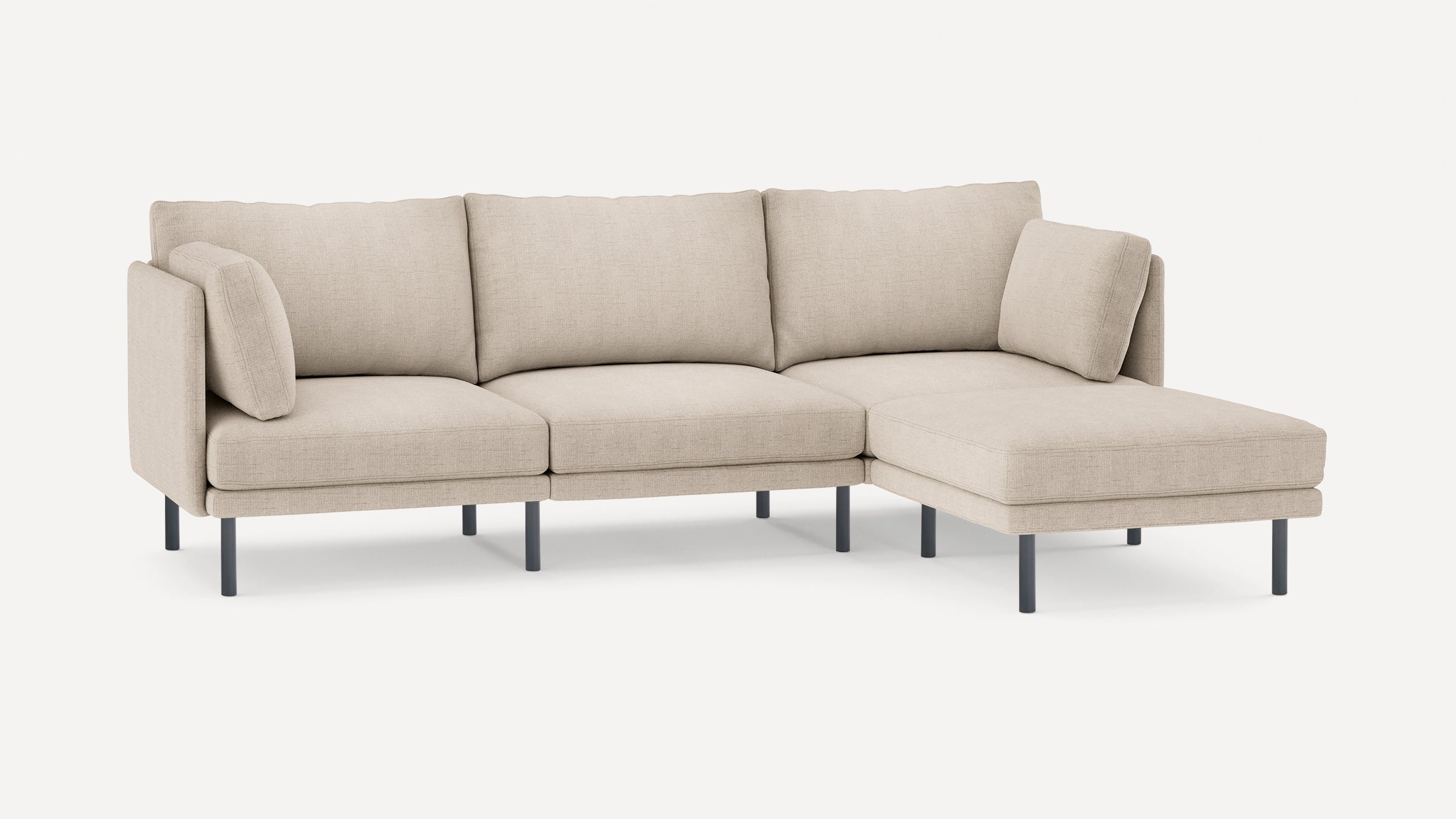 Beige sectional sofa with a right-facing chaise, cushioned seats, backrests, armrests, and slim black legs, shown on white background.