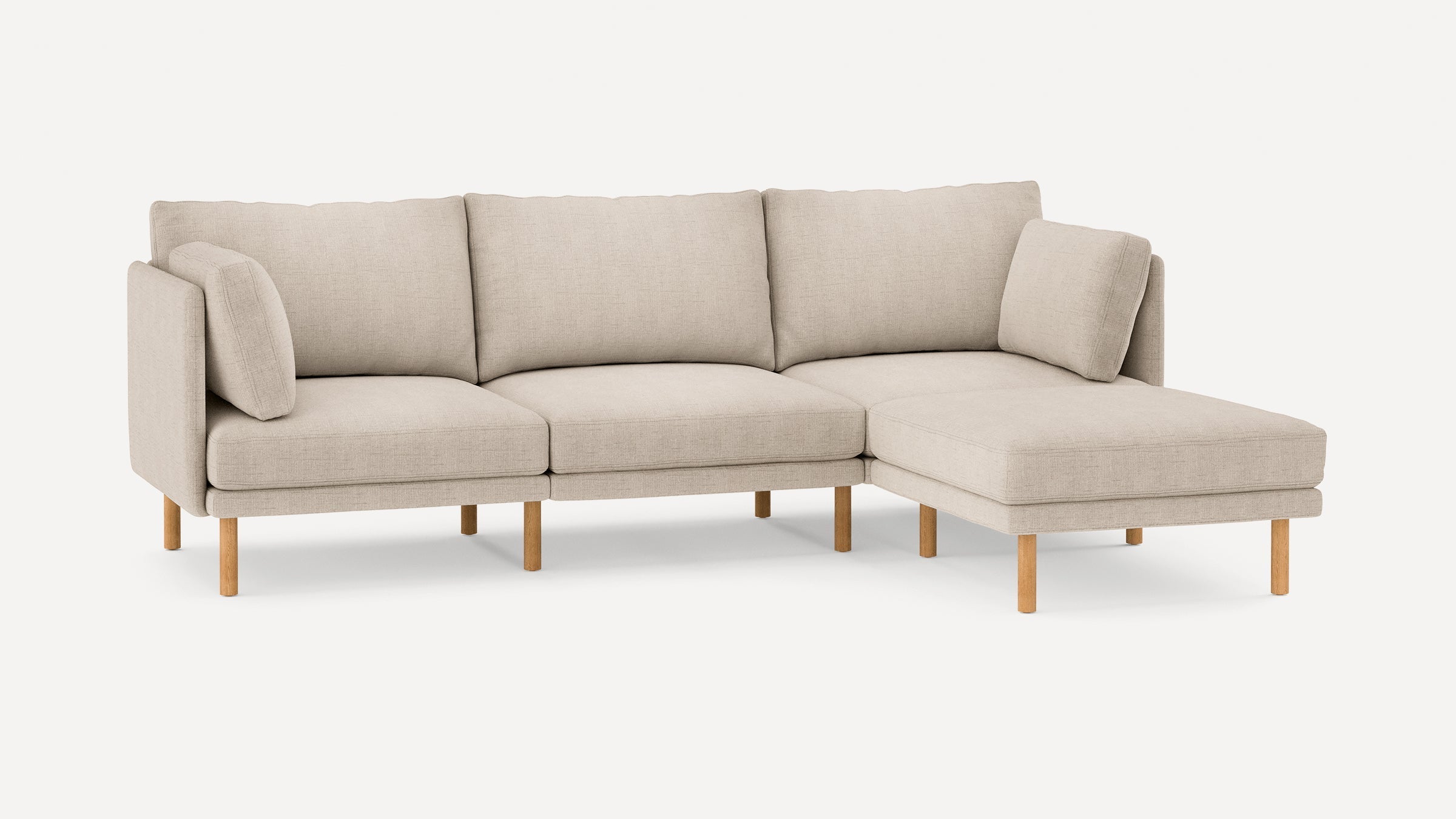 Beige L-shaped fabric sofa with wooden legs, featuring three back cushions and two armrest pillows for comfort.