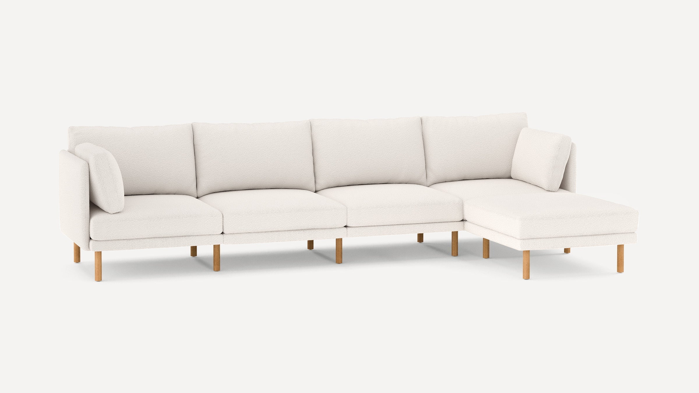 Modern white sectional sofa with soft cushions and wooden legs, featuring a chaise lounge on the right side.