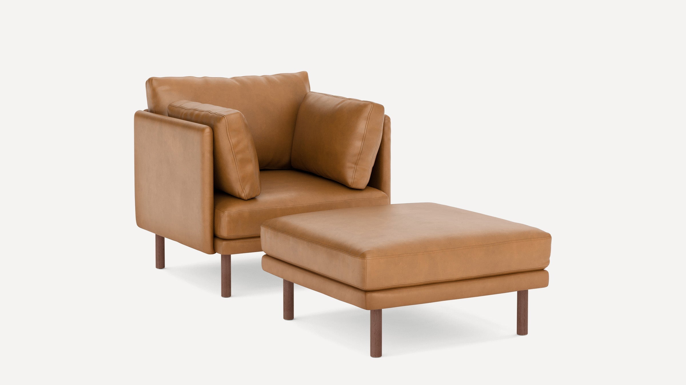 Modern tan leather armchair with two matching cushions and a separate ottoman, wooden legs on both pieces.