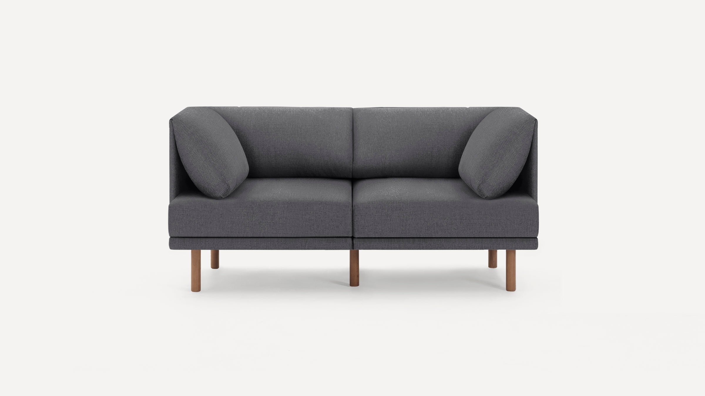 Modern two-seater sofa in dark gray fabric with angled cushions and wooden legs, minimalist design.