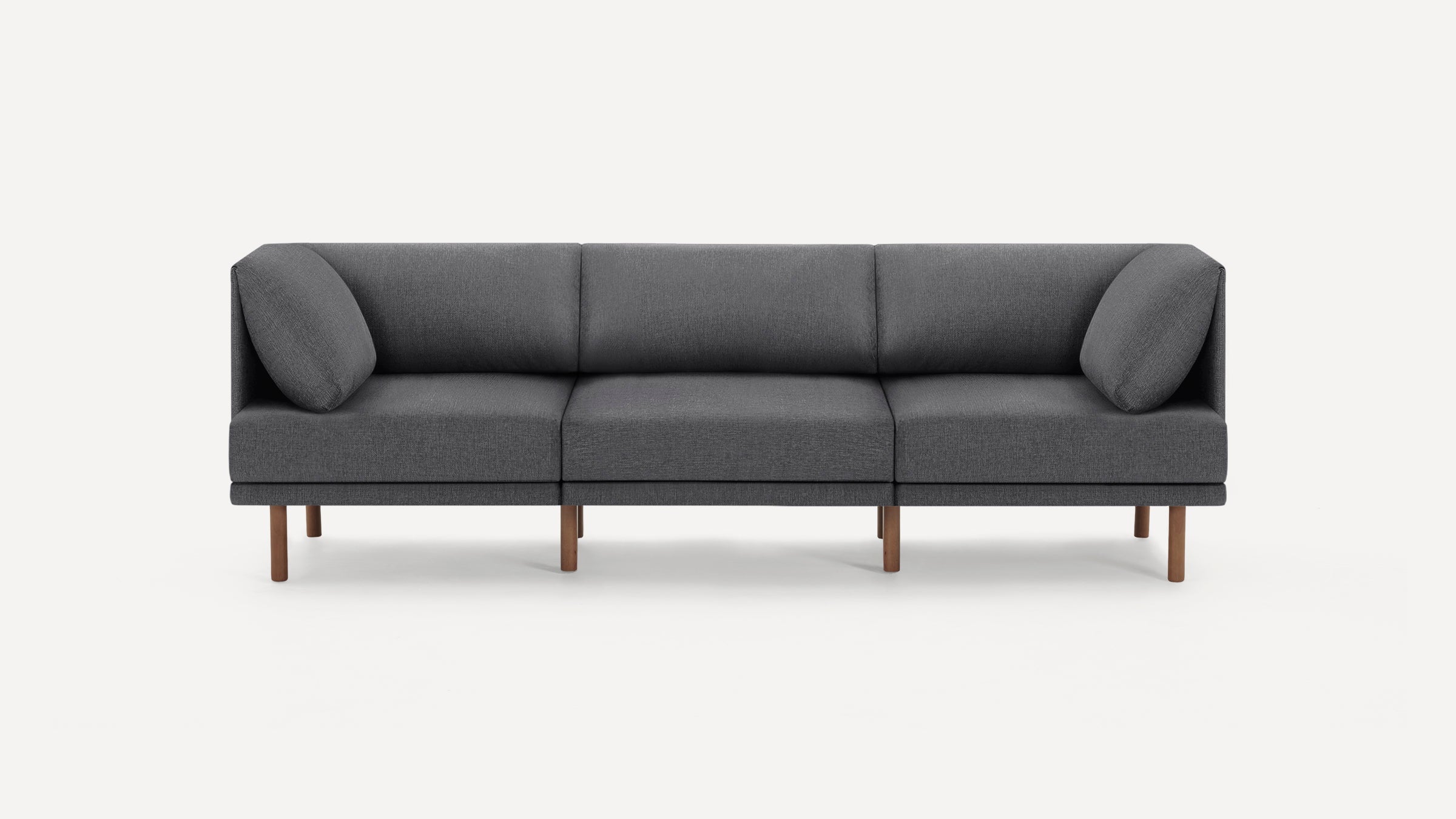 Modern three-seater sofa with dark gray fabric upholstery, wooden legs, and angled side cushions against a white background.