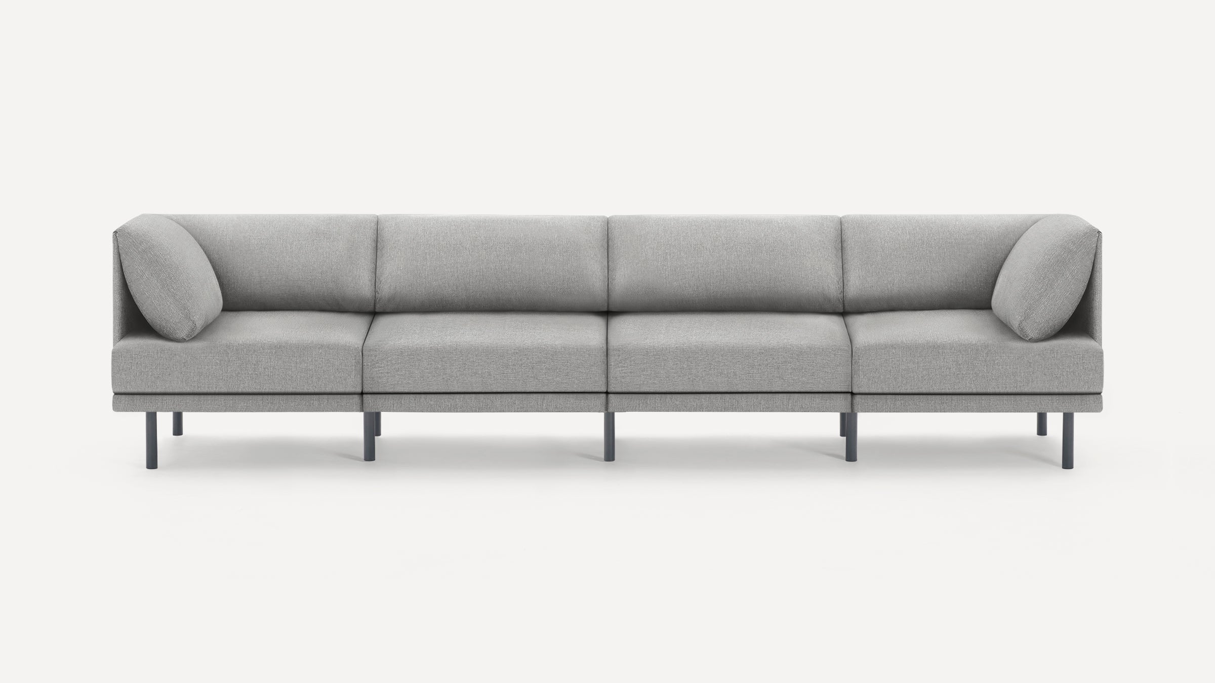 Modern, minimalist grey fabric four-seater sofa with slim black legs and two side bolsters on a white background.