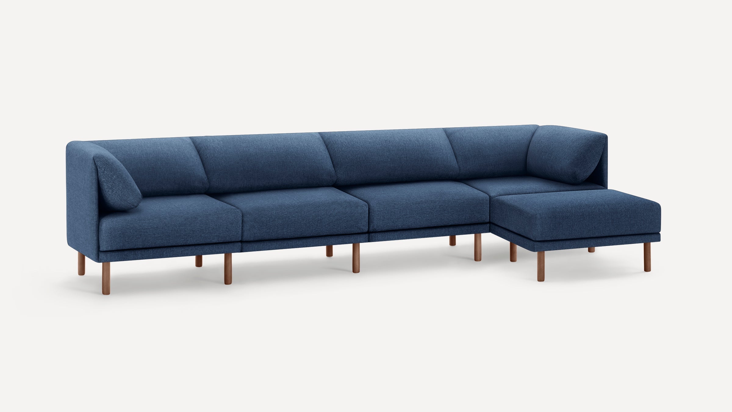 Modern sectional sofa with deep blue upholstered cushions, wooden legs, and an L-shaped design featuring a chaise lounge on the right side.