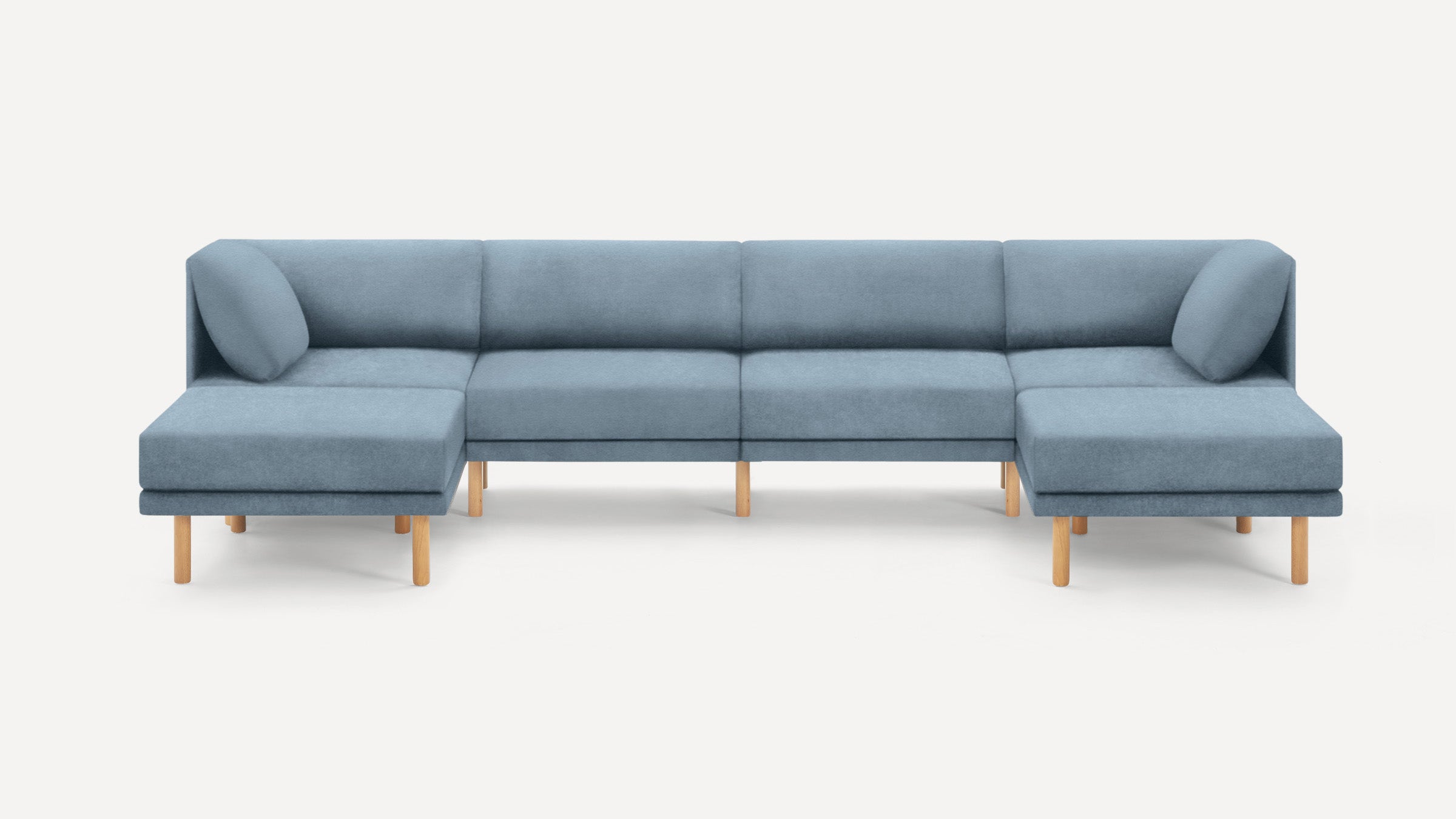 Modern light blue upholstered sectional sofa with wooden legs and two corner cushions on a plain white background.