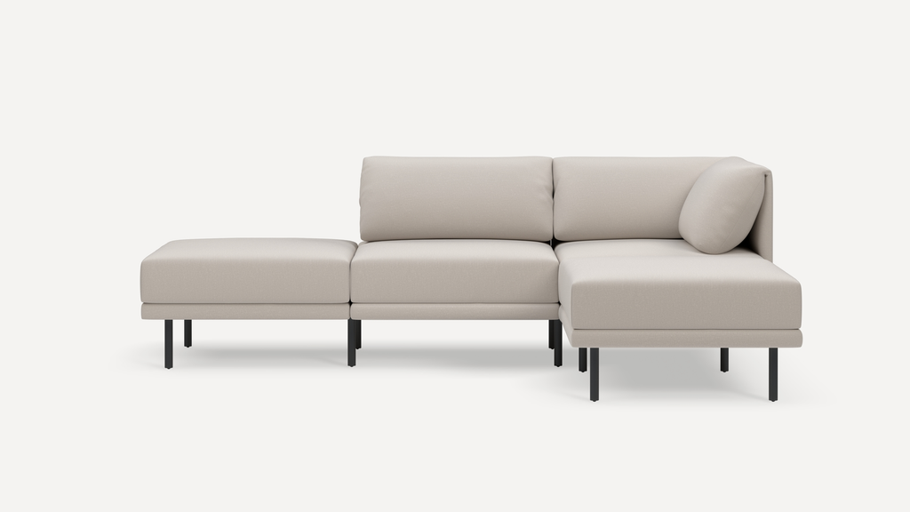 Light beige modern sectional sofa with three seat cushions, back cushions, and slim black metal legs on white background.