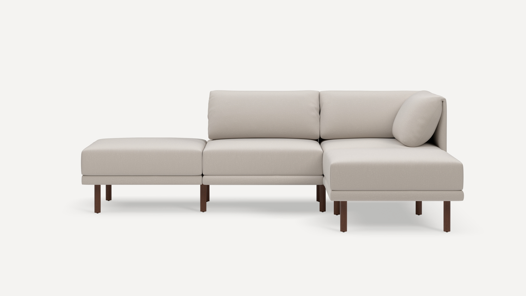 Beige modular sectional sofa with wooden legs, featuring two seats, a chaise lounge, and cushioned backrests against a plain white background.
