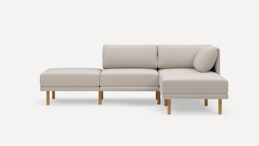 Beige modular sectional sofa with wooden legs, featuring three seating sections and an attached corner back cushion.