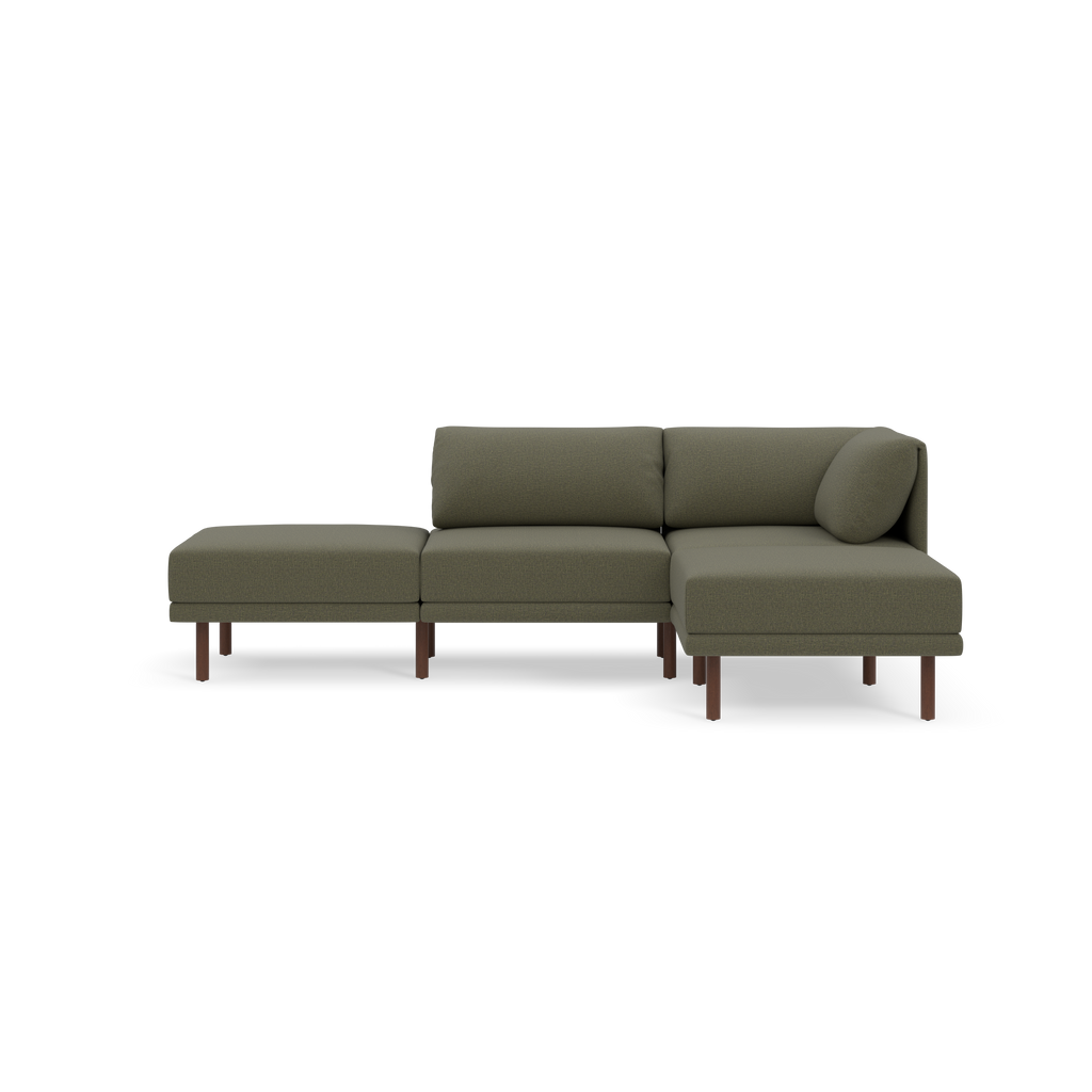 Modern Moss green fabric sectional sofa with wooden legs, featuring a chaise lounge and a round accent pillow, isolated on black background.