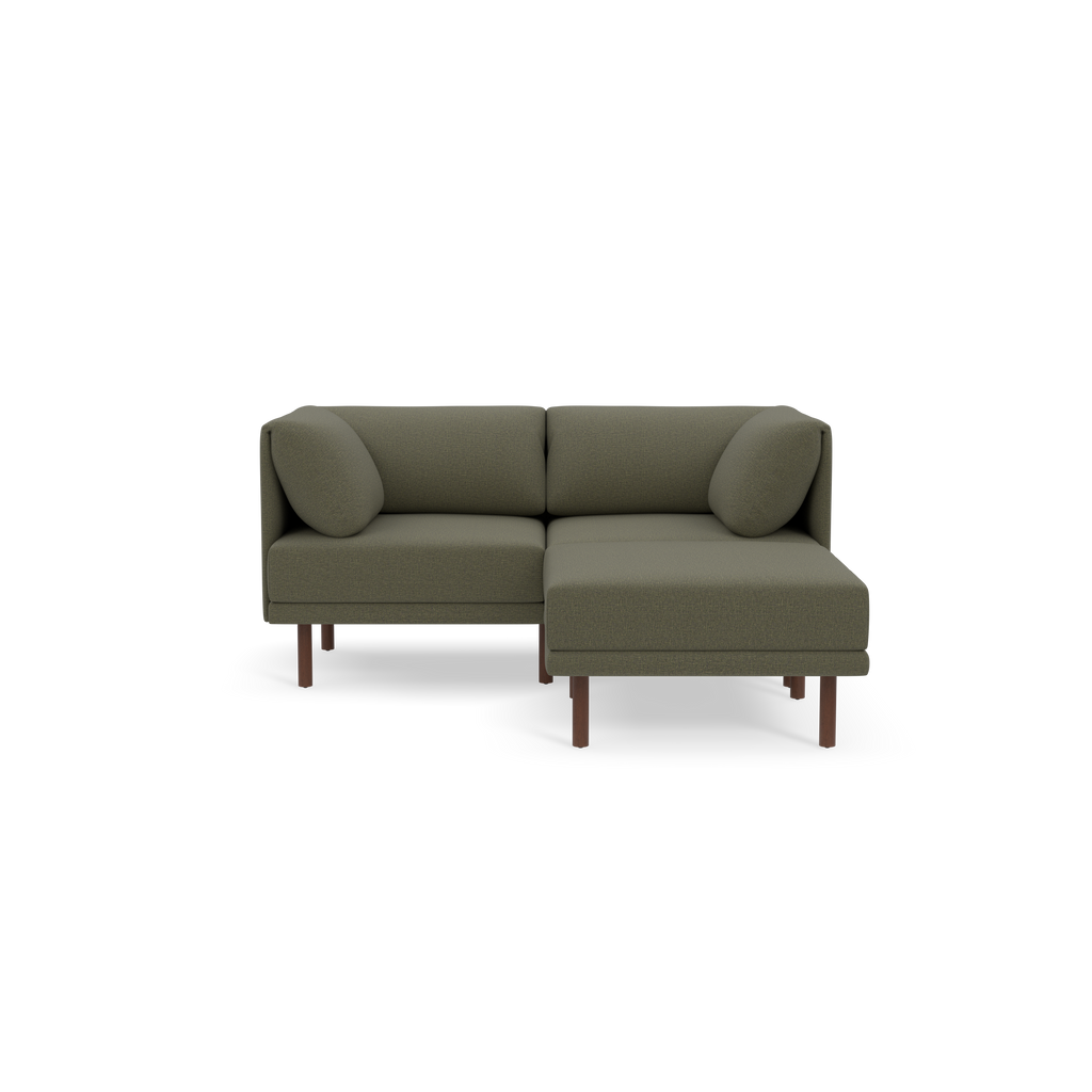 Modern Moss green L-shaped sofa with two matching cylindrical pillows and slim wooden legs on black background.