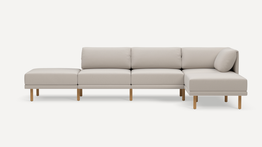 Light beige modern sectional sofa with clean lines, wooden legs, and three seat cushions plus an extended chaise lounge.