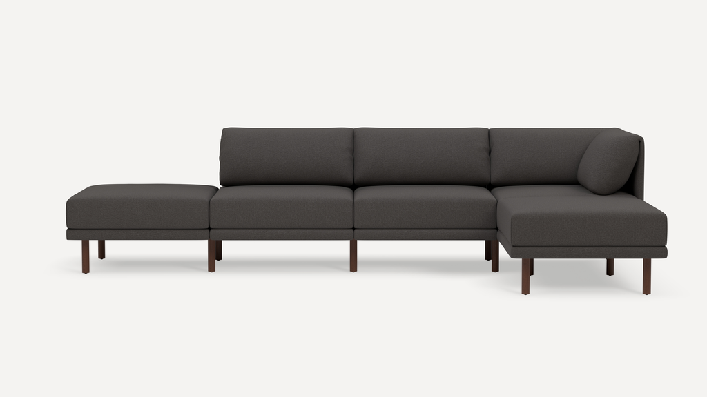 Modern dark gray sectional sofa with wooden legs, featuring an ottoman on the left and a chaise lounge on the right.