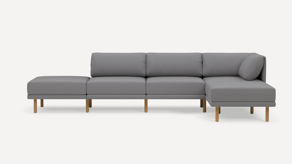 Modern gray sectional sofa with wooden legs, featuring a chaise lounge and cushioned backrest, isolated on white background.