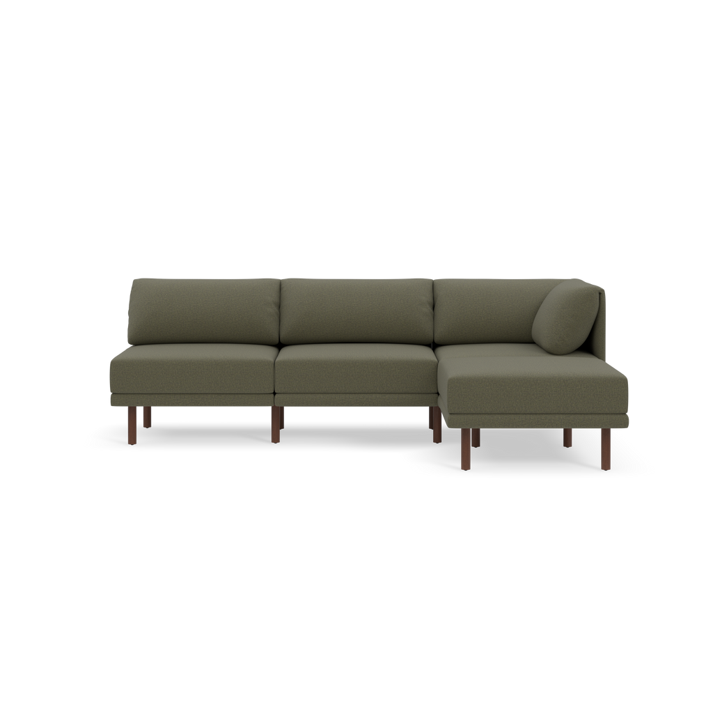 Modern L-shaped sectional sofa with Moss green fabric upholstery and slender wooden legs, featuring a round cylindrical pillow on one side.