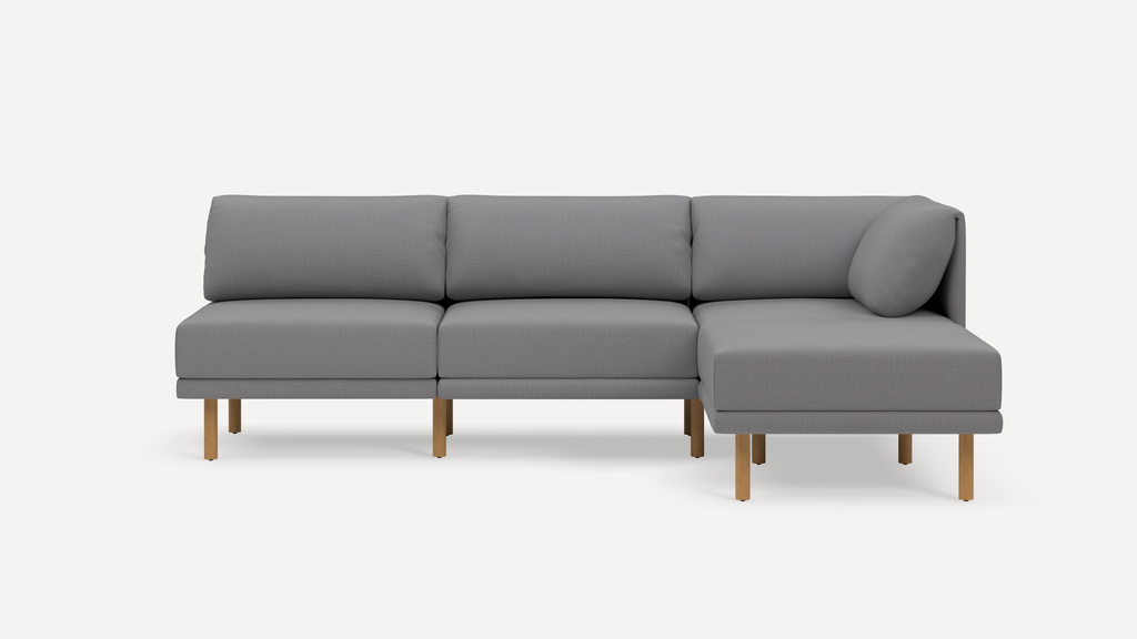 Modern gray fabric sectional sofa with wooden legs, featuring three seats and a chaise lounge on the right side.