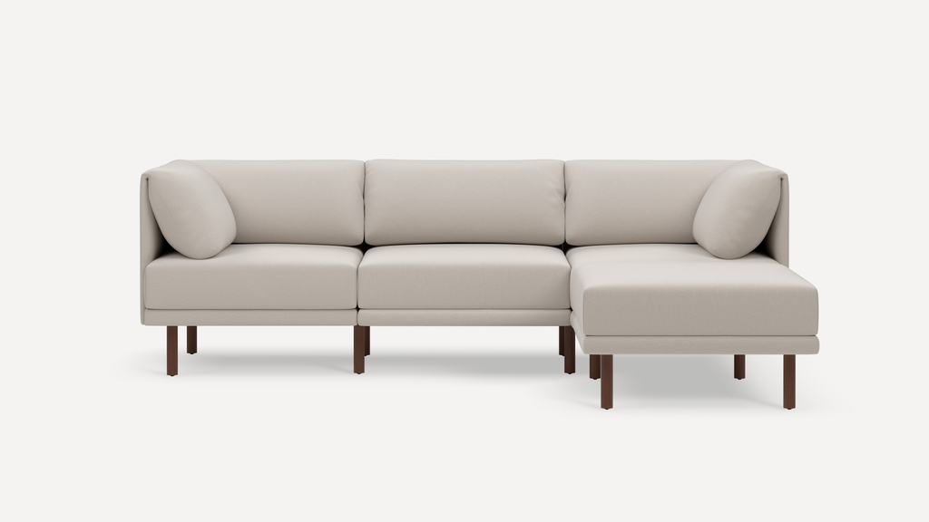 Modern light beige sectional sofa with wooden legs, three back cushions, and two side pillows on a white background.