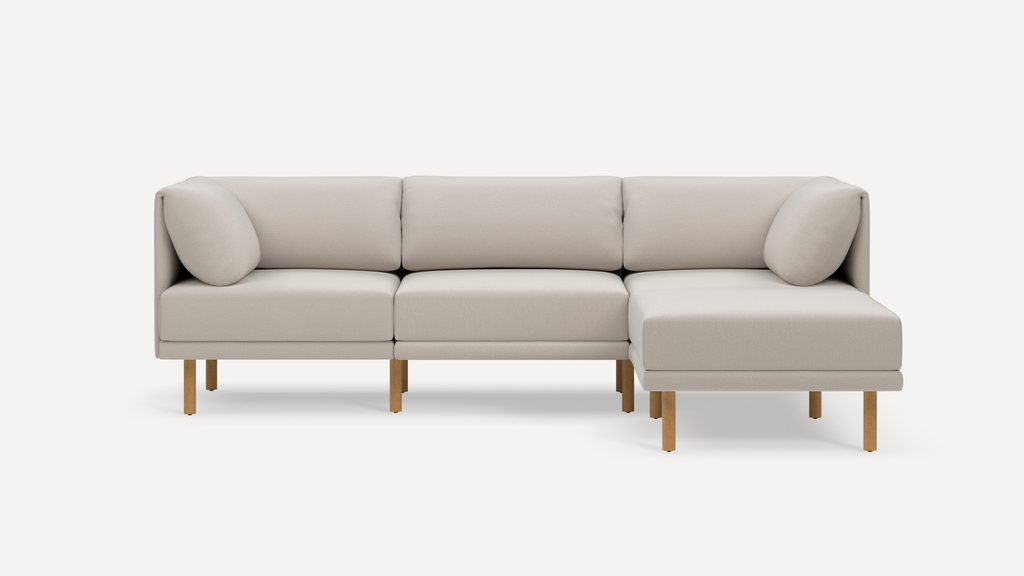 Beige L-shaped modern sectional sofa with a right chaise, wooden legs, and two cylindrical cushions on each end.