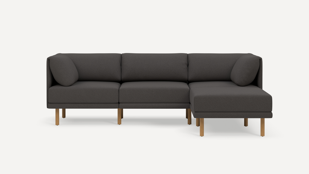 Modern dark gray sectional sofa with wooden legs, featuring three seats and a chaise lounge on the right side.