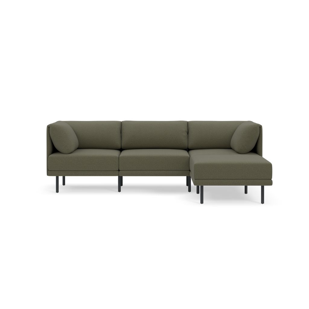 Modern Moss green L-shaped sectional sofa with slim black legs and two cylindrical side cushions, set against a black background.