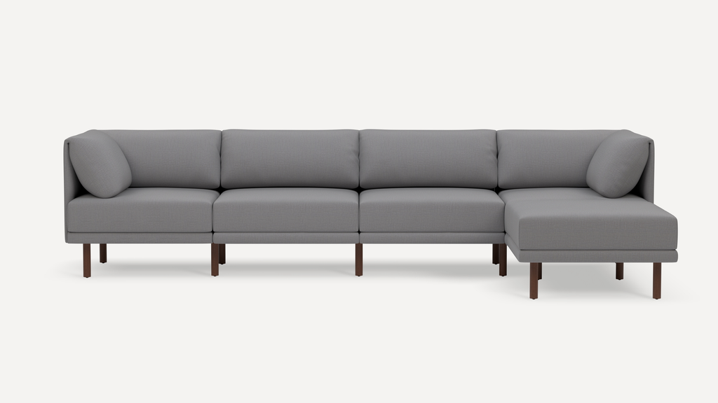 Modern gray fabric sectional sofa with wooden legs, featuring four seat cushions and two cylindrical arm pillows.