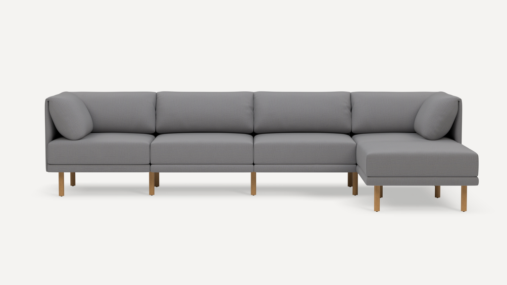 Modern L-shaped sectional sofa with light gray fabric upholstery and wooden legs, featuring plush back cushions and rounded armrests.