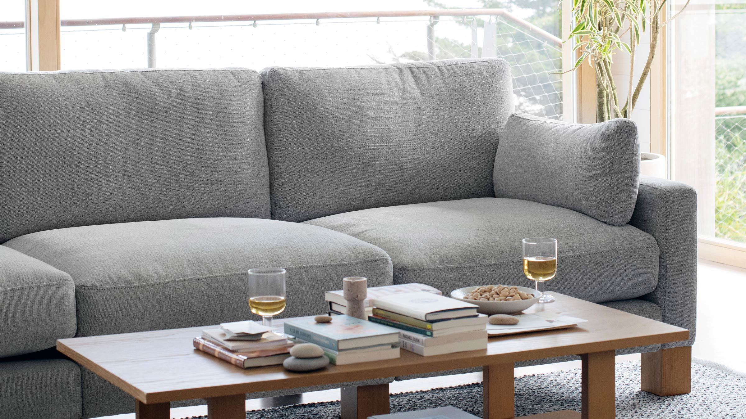Light gray fabric sectional sofa with cozy cushions next to a wooden coffee table holding books, snacks, and two glasses.